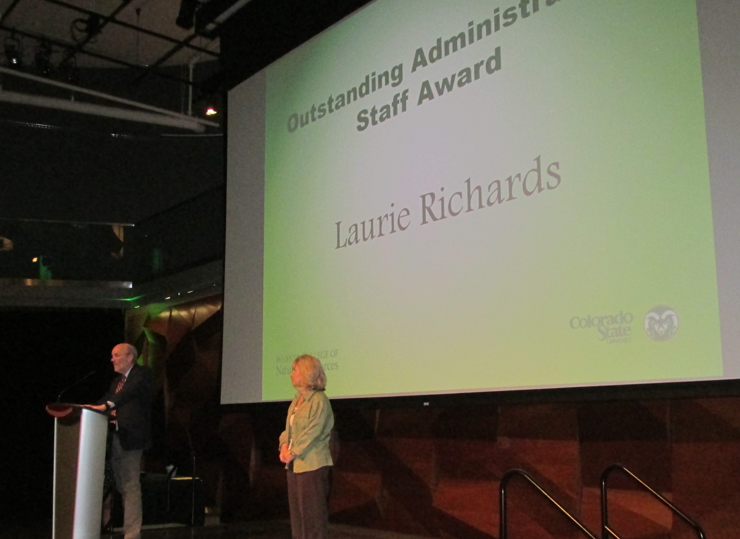 Laurie poses on stage in front of the screen presenting her with her administrative award.