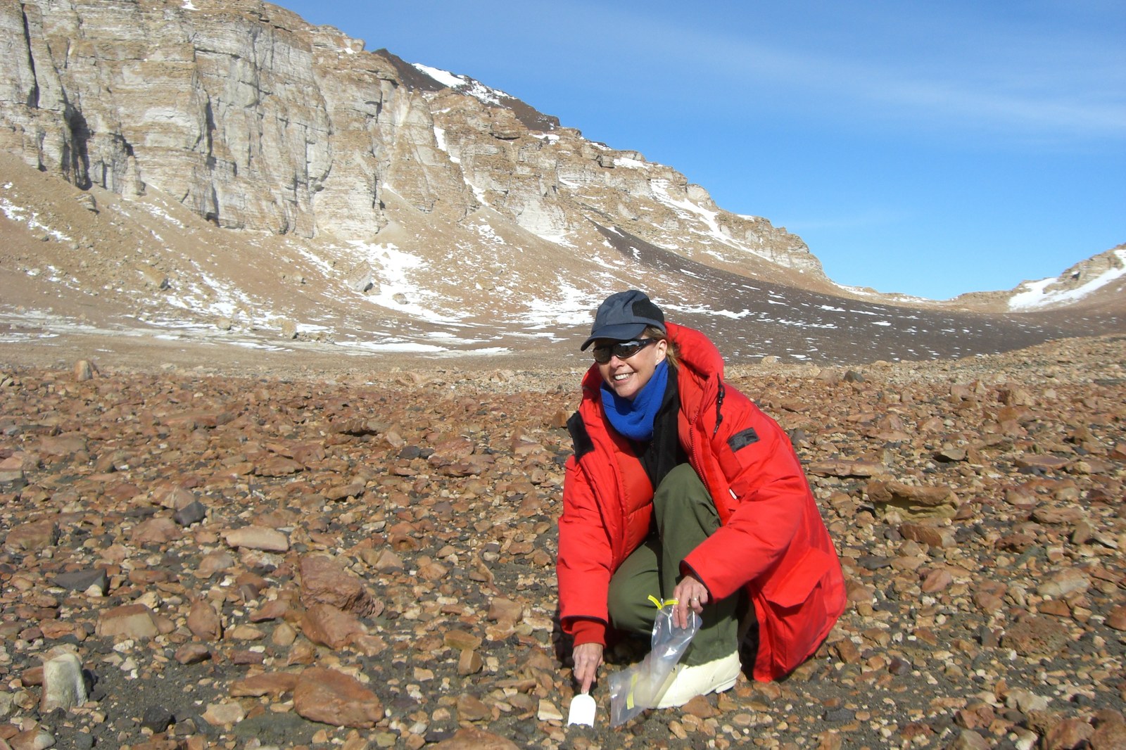 Ecologist Diana Wall kneeling to collect soil samples for nematode research on the barren terrain of the Antarctic Dry Valleys.
